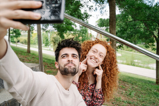 Young Couple Making Cute Faces While Talking Selfie In Public Park