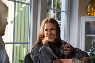 Happy girl with glass of water looking at mother in dining room