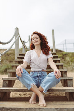 Redhead woman meditating while sitting cross-legged on steps