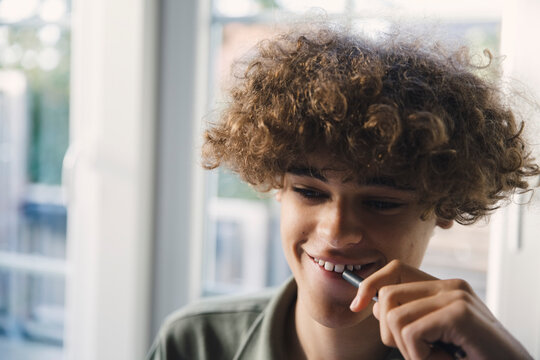 Smiling teenage boy biting pen at home