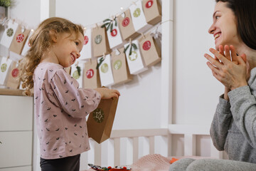 Mother with child opening Christmas advent calendar tasks and gifts. Toddler girl excited about...