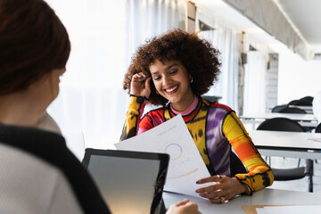 Smiling woman reading document while studying with friend at university