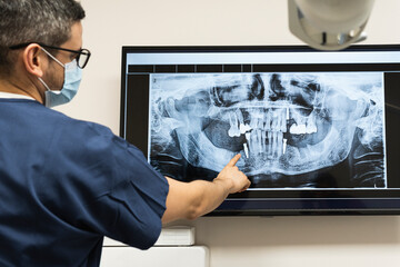 Male dentist wearing protective face mask examining dental x-ray at clinic