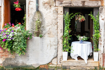 Fototapeta na wymiar Windows of Italian restaurant full of flowers facing canal in Venice, Italy