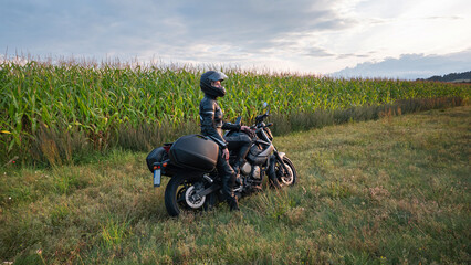 Fototapeta na wymiar sense of adventure she and her motorcycle resting for a moment on the side of a rural road of sun-drenched agricultural fields in the golden hour