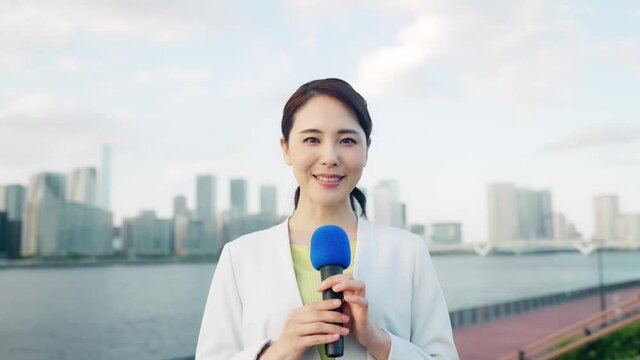 都市の前に立つ女性アナウンサー 60p