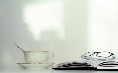 The open diary lies on a white background. On the pages are white-framed glasses. There is a coffee cup with a spoon nearby