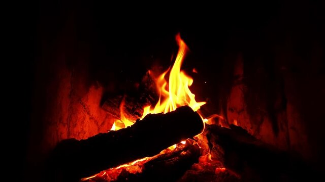 Closeup footage of the fireside in a stone cave with burning flame filmed in slow motion. A cozy place for spending warm romantic evening. Logs and embers are glowing in darkness. Relaxing atmosphere.