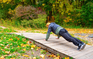 Pushups. Stylish hair dyed man doing push ups in the autumn park. Open air training concept.