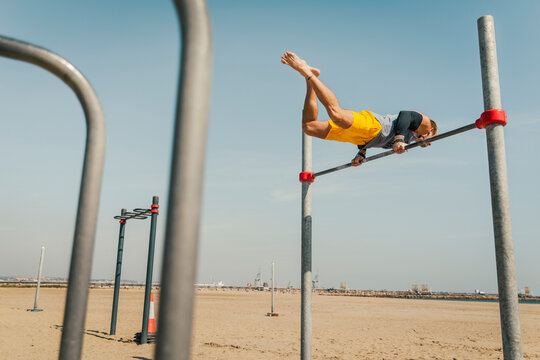 Male athlete balancing on high bar on beach