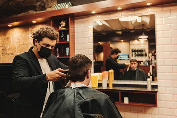 Male barber using clipper while cutting customer's hair in salon during pandemic