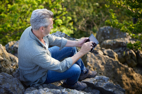 Man using digital tablet while sitting on mountain