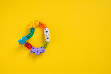 Top view a colorful baby rattle on yellow background with copy space. Flat lay newborn rattle toy on colored background. Baby toys concept