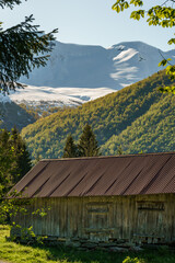 Old grey farm house with mountains covered with snow in the background.