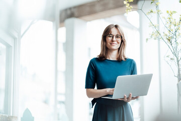 Female business professional holding laptop while standing in cafe