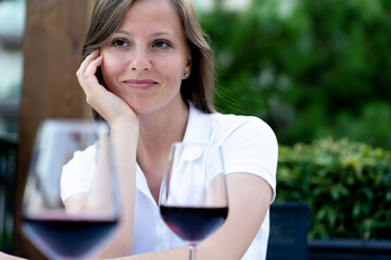 Portrait of a beautiful sexy woman in a white dress, drinking wine in a summer restaurant on the veranda and looking into the eyes of her boyfriend companion. romantic meeting date setting on