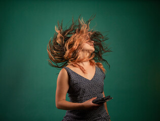 Young woman with mobile phone tossing hair against green background