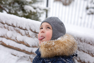A little boy tries to catch snowflakes with his tongue in the winter on the street. He is having fun.