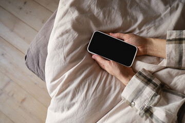 Hand holds smartphone in bed close-up. The girl reaches for her mobile phone to turn off the alarm or read a message. The man fell asleep with a phone in his hand