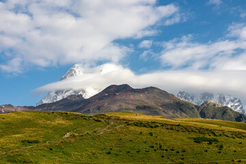 Obraz premium Panoramic view on the Ushba mountain peaks covered by clouds near Mestia in the Greater Caucasus Mountain Range, Upper Svaneti, Country of Georgia. Hiking trail to the Koruldi Lakes. Wanderlust.