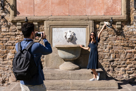 Man photographing woman standing by fountain through camera on sunny day