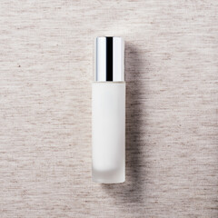 White cosmetic product in glass bottle with chrome cap on linen background