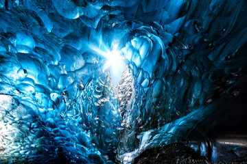  Blue glacial ice with hole through to the sky with sunburst, from an ice cave in the glacier. Vatnajokull glacier in southeast Iceland.