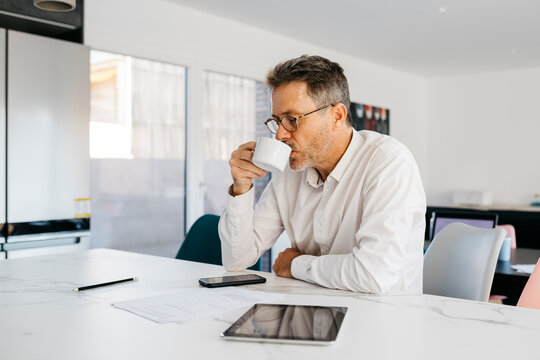 Businessman drinking coffee while sitting at kitchen island in home office