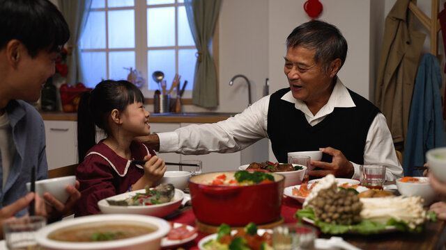 smiling senior man grandfather talking with hand gestures as the girl granddaughter giving food to him at the family reunion dinner party on the eve of Chinese new year
