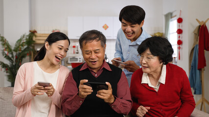 senior parents and adult son and daughter in law enjoying playing mobile phone games together on...