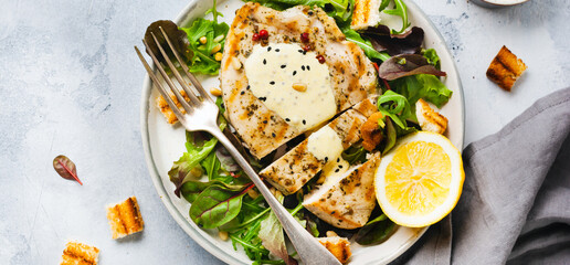 Homemade grilled turkey steak with sauce, broccoli, arugula and chard in a ceramic plate on a light concrete background. Top view.