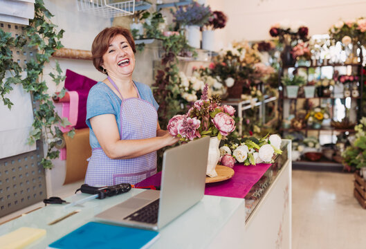 Cheerful female entrepreneur with brown hair arranging flowers while standing in shop