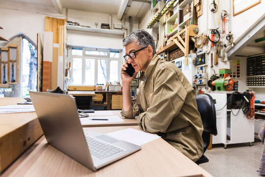 Male owner talking on mobile phone at table in workshop
