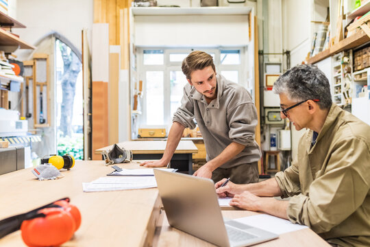 Male carpenter discussing with coworker while writing on paper at workshop