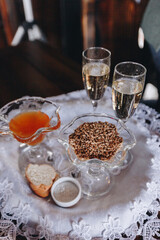 there are two glasses of champagne, plates with honey and seeds, bread and salt according to the Slavic wedding tradition on a tray served with a,  white napkin with embroidery close-up 