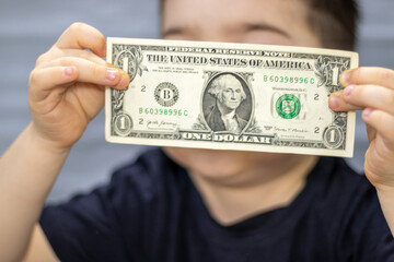 one dollar bill in front of kid child boy face cover eyes or mouth.dollars banknote in blue jeans pants pocket or isolated gray paper.financial education in school,money savings investment loans