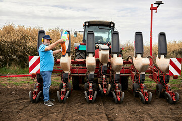 Male farmer wearing ear protectors while pouring corn in containers of tractor at agricultural field