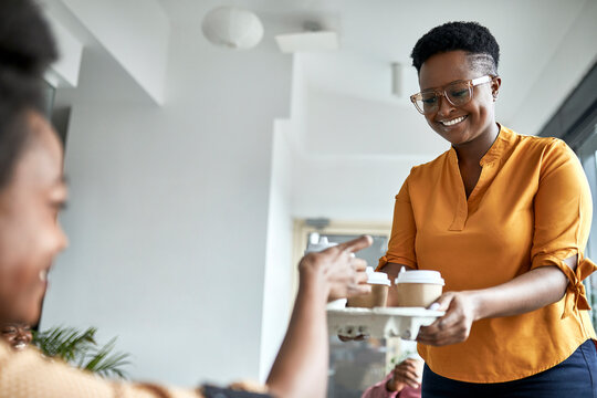 Smiling female entrepreneur offering coffee to female colleague at coworking office