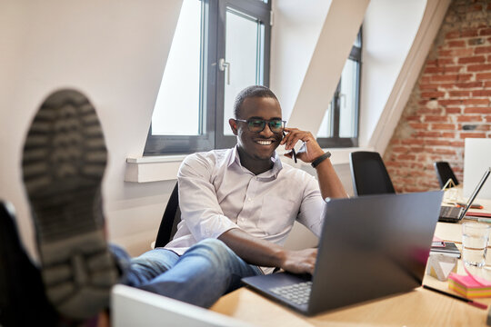 Male entrepreneur talking on smart phone while using laptop at office