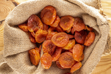 Several sweet dry apricots in a jute bag, close-up on a wooden table, top view.