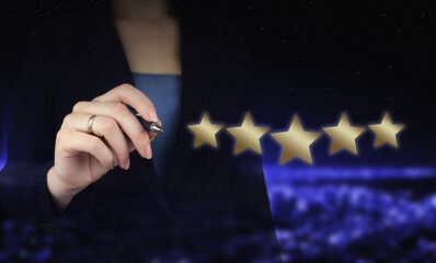 Hand pointing five star symbol to increase rating of company. Hand holding digital graphic pen and drawing digital hologram five stars sign on city dark blurred background.