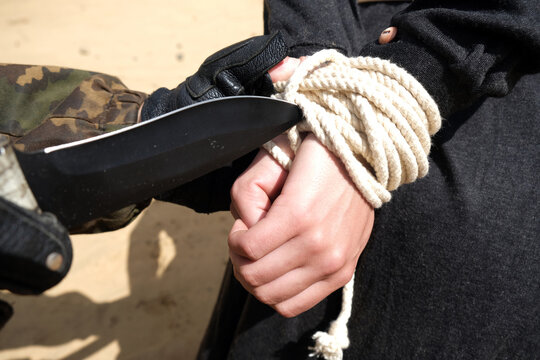 A gunman cuts the rope on the hands of a tied young woman with a knife
