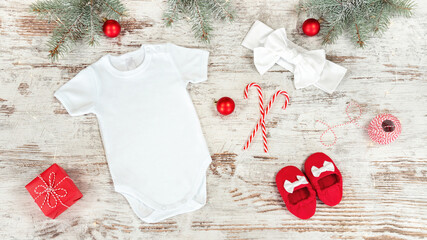 Newborn baby clothes mockup complete with booties and headband on christmas background with fir brahches. Infant romper and nursery accessories on background with Christmas toys, candy canes.