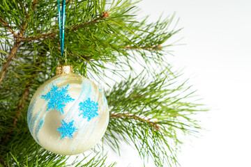 White or cream glass Christmas ball with a pattern of blue snowflakes and glitter hangs on the...