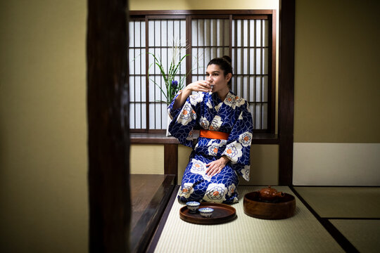 Japan, Young woman wearing traditional kimono drinking tea in ryokan