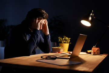 Tired businessman sitting at desk while working late night at home