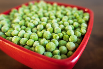 frozen frosty green peas in red ceramic bowl closeup