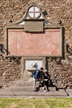 Tourists checking map in front of fountain wall on sunny day