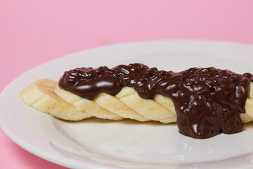 Banana in chocolate on a pink background. Banana slices are drizzled with melted chocolate on a white plate. Fruit dessert