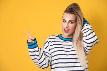Surprised young woman pointing with forefinger to copy space for your text or image, isolated on yellow background. I know, this secret is discovered